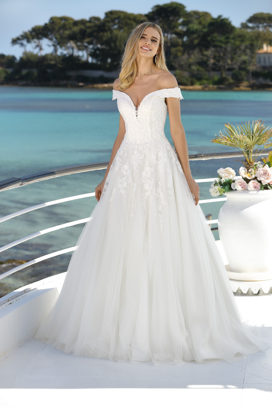 Ladybird Hochzeitskleider in klassischer A Linie - Modell 421002. Das schulterfreie Brautkleid ist mit feinsten abfließenden Spitzenapplikationen am Oberteil und Rock gearbeitet. Der dekorative Carmenausschnitt ist sehr sexy und der weite Organzarock schwingt bei jedem Tanzschritt mit